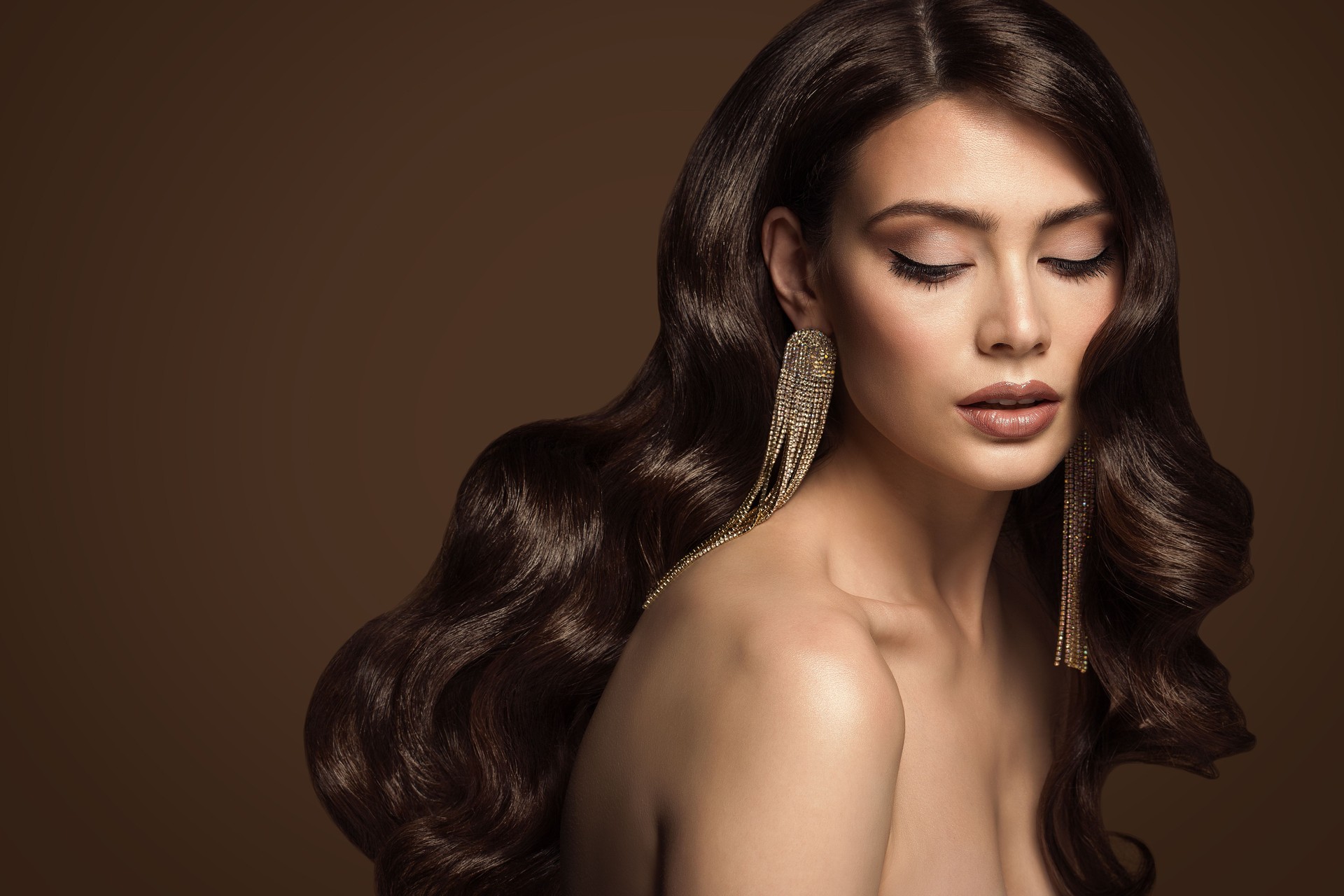 Brunette Model with Long Shiny Waving Hairstyle. Luxury Hair Care. Beauty Woman Natural Face Make up over Brown Studio Background